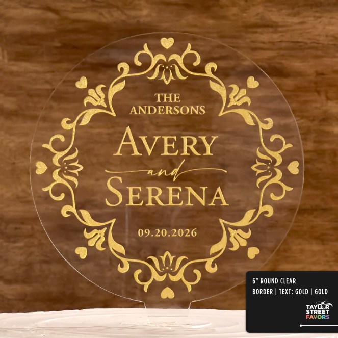 A round acrylic cake topper with elegant gold scroll work design and heart accents on the border. In the center, the customizable text reads: “THE ANDERSONS” at the top, followed by “AVERY and SERENA” in large, bold letters, and “09.20.2026” at the bottom. The background is a warm wood texture, and the topper is displayed on a white cake.